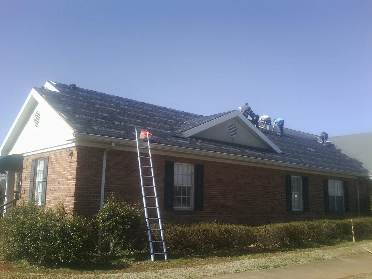 Crew tearing shingles off a brick ranch roof with a ladder set — Metal Roof Repair work by our crew in Knox
