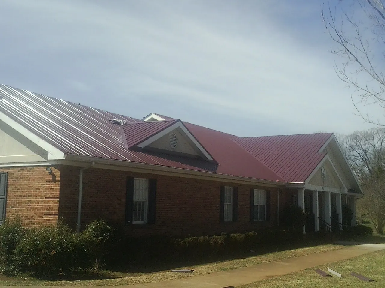 Red metal roof with gabled entries on a long brick building, from a Hail Damage Roof Repair job in Knox