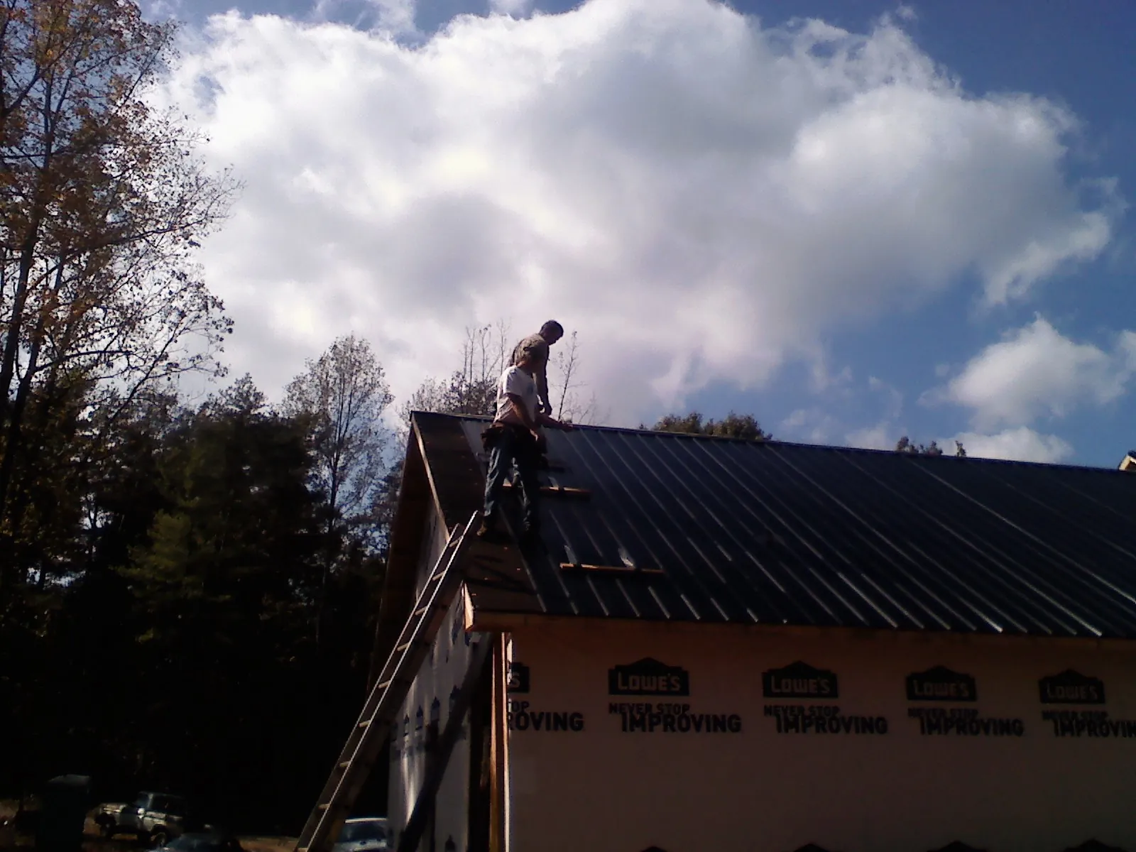 Roofer fastening dark metal panels high against a cloudy sky, from a Roof Inspection job in Knox