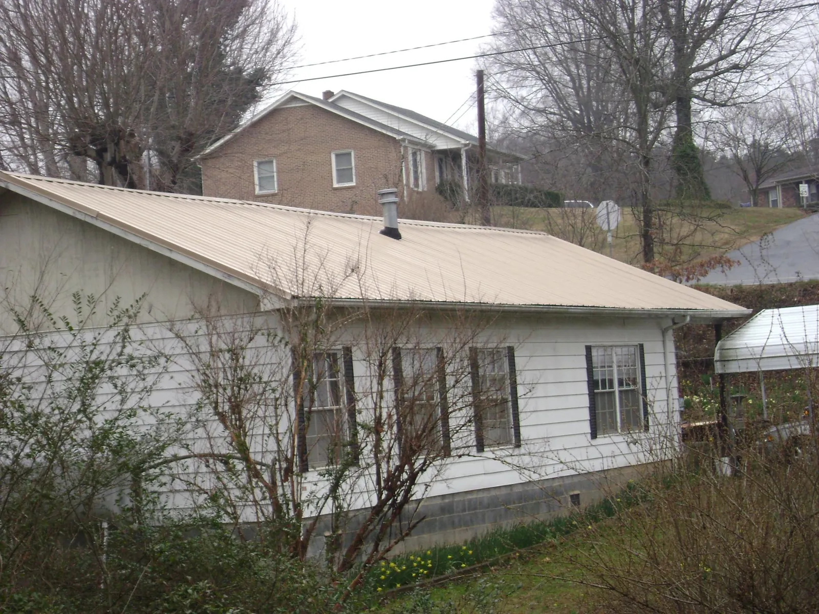 Tan metal roof on a white sided house set into a hillside — Commercial Roofing by Roofing Brothers in Knox