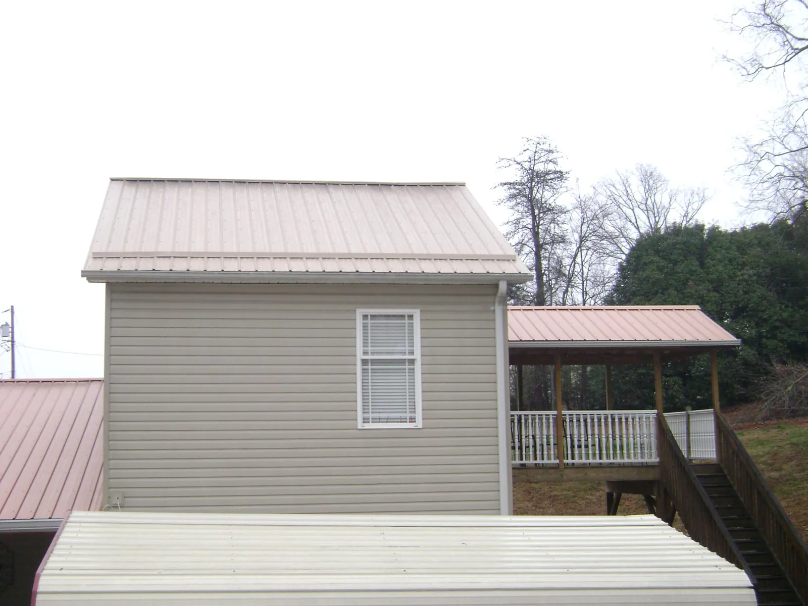Tan metal roofs on a two story addition and attached porch, from a Roof Replacement job in Knox